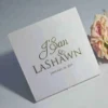 Satin wedding invitation box with gold foil names and date, styled beside blush pink roses