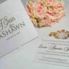 Satin invitation box lid beside its matching gold foil acrylic wedding invitation card and roses