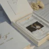 Open ivory velvet invitation box with the lid raised, a clear acrylic invitation in gold foil over a couple’s photo, and a pocket for enclosure cards in the lid.