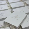 Top view of several ivory velvet wedding invitation boxes with gold foil monograms arranged in rows, showing a bulk order of luxury monogram invitation boxes.