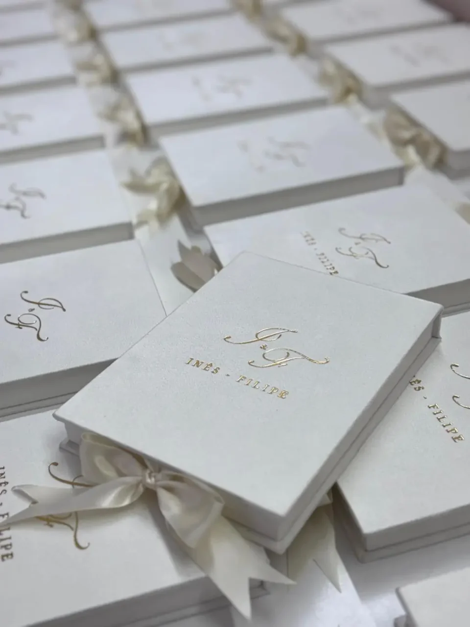 Top view of several ivory velvet wedding invitation boxes with gold foil monograms arranged in rows, showing a bulk order of luxury monogram invitation boxes.